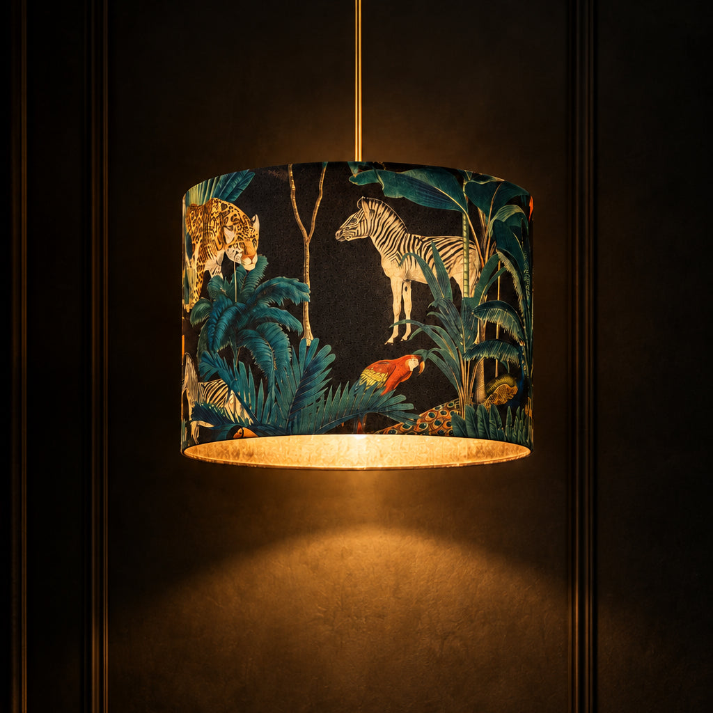 A table lamp with a cylindrical drum shade featuring a blue and teal jungle print with zebra, giraffe, and toucan motifs, mounted on a rustic three-legged wooden tripod base.