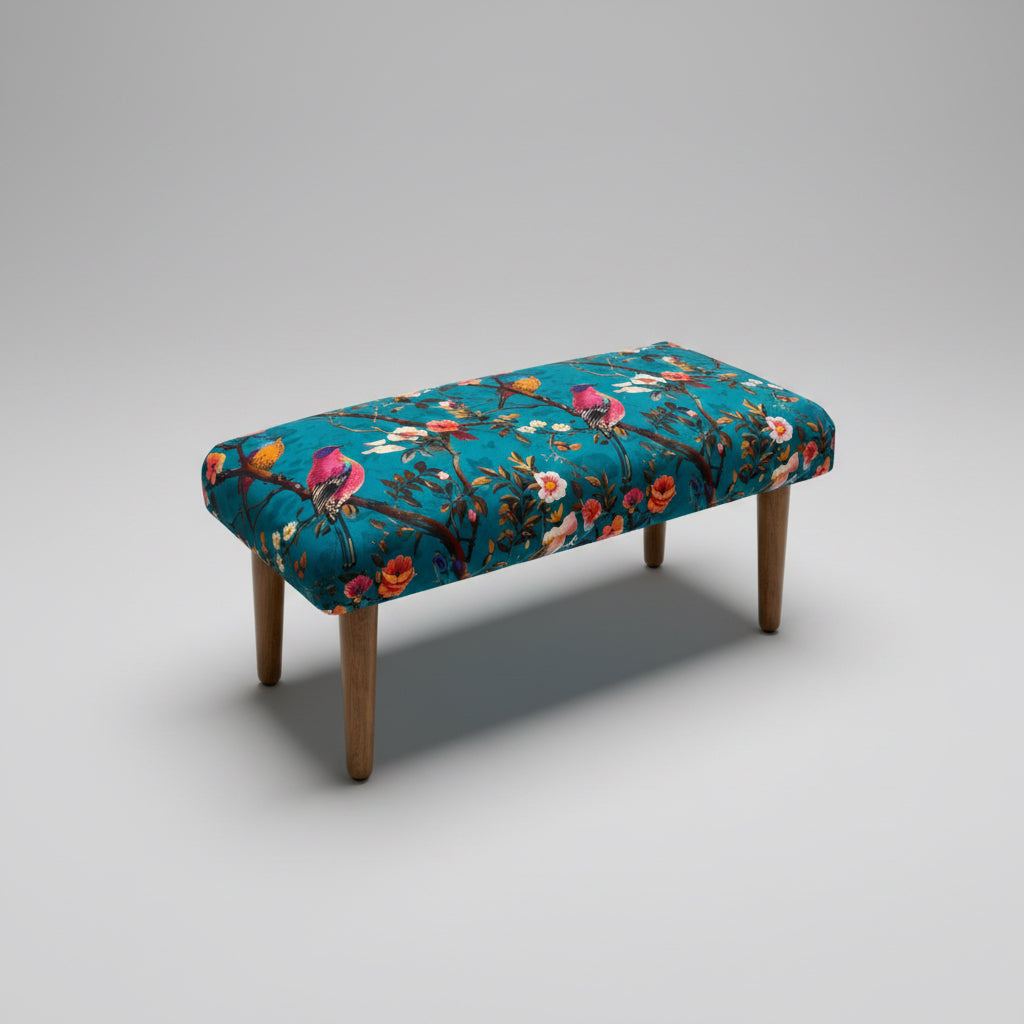 A rectangular upholstered bench with a vibrant teal floral pattern and four tapered wooden legs, shown on a neutral gray studio background.