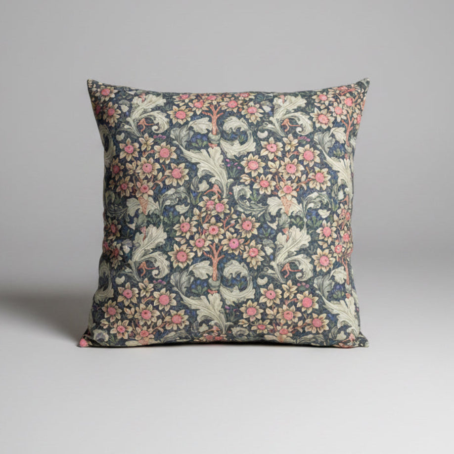 A square decorative throw pillow featuring a vintage-style floral and botanical pattern in muted pink, cream, and slate blue-gray tones, set against a neutral gray studio background. William morris orchid